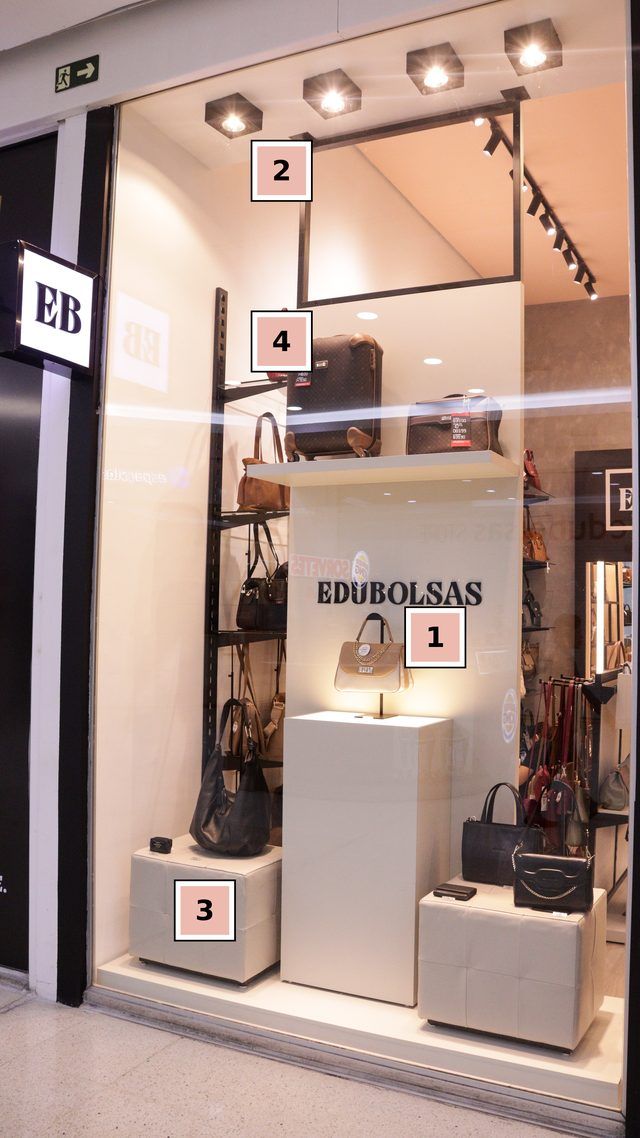 Vitrine da loja Edubolsas com uma bolsa em destaque no centro, iluminada, e cubos mais baixos nas laterais